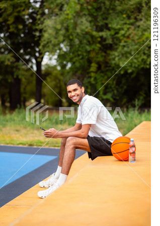 Young attractive man with a ball sitting with a gadget in hands 121196309