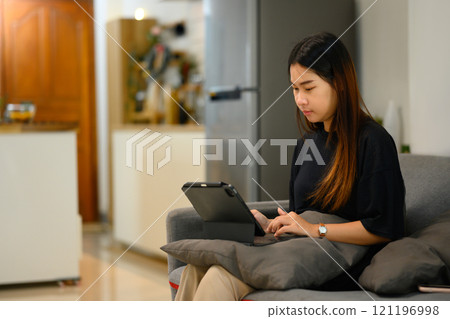 Focused young woman working on a digital tablet in living room Focused young woman working on a digital tablet in living room 121196998