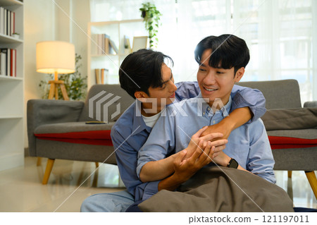 Cheerful gay couple embracing and smiling at each other in a stylish living space Cheerful gay couple embracing and smiling at each other in a stylish living space 121197011