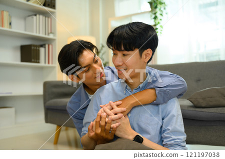 Loving LGBTQ embracing affectionately and smiling warmly in a cozy living room Loving LGBTQ embracing affectionately and smiling warmly in a cozy living room 121197038