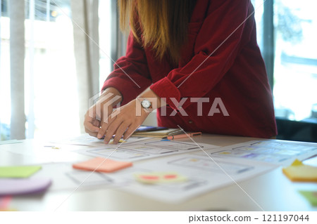 Close up of female designer arranging wireframe designs on desk covered with sketches and sticky notes 121197044