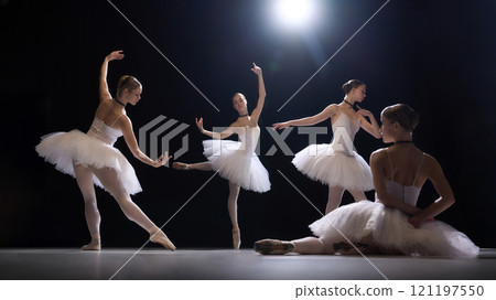 Four graceful ballerinas, young girls in white tutus performing elegant and artistic dance movements on dimly lit stage. Beauty of ballet. 121197550