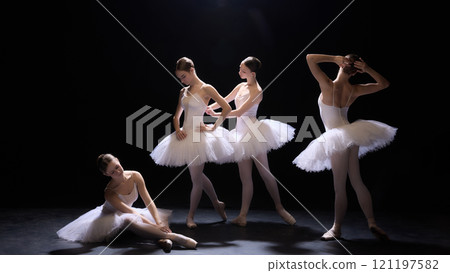 Four young graceful young ballet dancers, girls in beautiful white tutus standing in elegant pose, performing on dimly lit stage. Four young graceful young ballet dancers, girls in beautiful white tutus standing in elegant pose, performing on dimly lit stage. 121197582