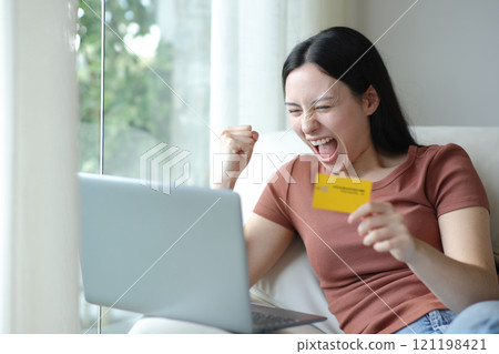 Excited asian woman buying online with laptop and card 121198421