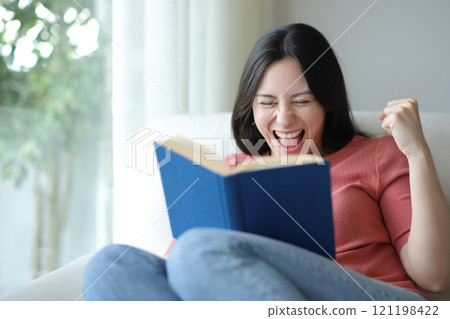 Excited asian woman celebrating book argument at home Excited asian woman celebrating book argument at home 121198422