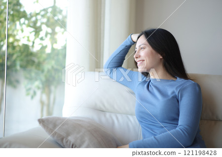 Happy asian woman relaxing looking through a window at home 121198428
