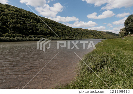 Serene Landscape of a River Bordered by Lush Green Hills Under a Cloudy Sky Serene Landscape of a River Bordered by Lush Green Hills Under a Cloudy Sky 121199413