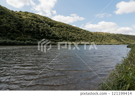 Serene River Landscape Surrounded by Lush Green Hills Under a Blue Sky 121199414