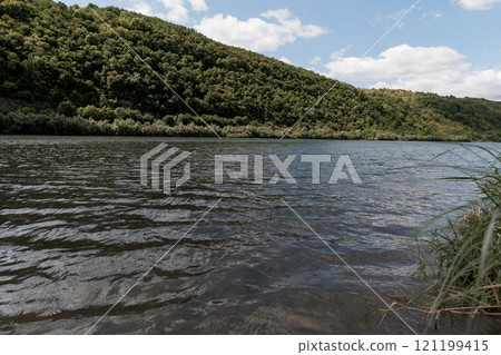 Serene Riverbank Landscape with Lush Green Hills Under a Bright Sky 121199415