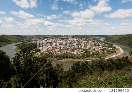 Panoramic View of a Serene River Town Surrounded by Lush Hills Panoramic View of a Serene River Town Surrounded by Lush Hills 121199420