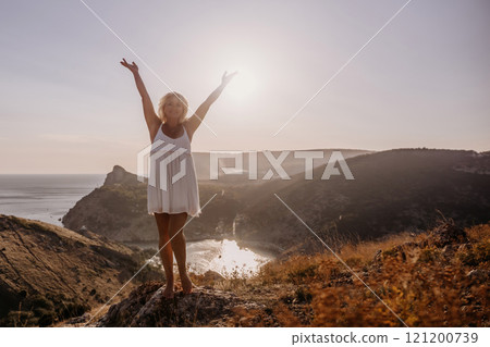 woman standing hill with her arms raised in the air, looking up at the sun. The scene is peaceful and serene, with the woman's expression conveying a sense of joy and happiness. 121200739