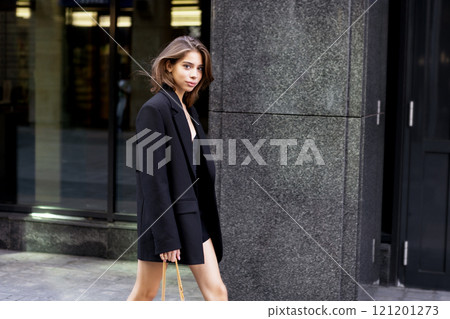 Fashionable young woman wearing elegant outfit oversize black blazer, beautiful model with dark hair Walking urban city. Modern fashion, street style 121201273