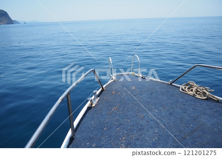 Calm waters stretch endlessly under a clear blue sky. Boat foreground showcases worn details while distant hills create tranquil backdrop. RT Dubovica Rocks near Buljarica, Svetac Rock, Montenegro. 121201275