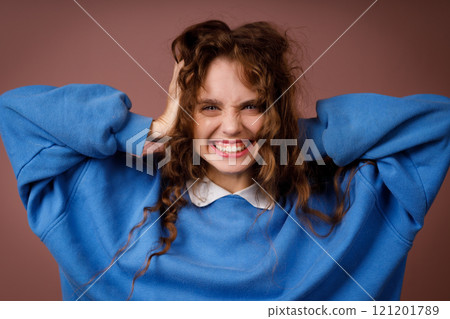 Happy surprised young adult woman wearing winter blue sweater and hold head with her hands looking at camera with joyful smile Happy surprised young adult woman wearing winter blue sweater and hold head with her hands looking at camera with joyful smile 121201789