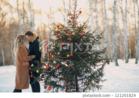 Young adult couple man and woman decorates pine tree in winter park forest. New year tree holiday party celebration concept 121201829