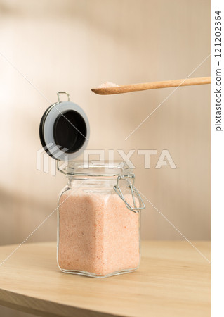A jar of Himalayan salt sits on a table, with a wooden spoon scooping some. 121202364