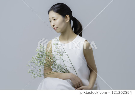 Portrait of a young woman wearing a white dress and holding flowers against a gray background Portrait of a young woman wearing a white dress and holding flowers against a gray background 121202594