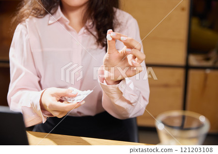 Cropped photo of young woman holding pill blister ready to drink it sitting at table at office. Cropped photo of young woman holding pill blister ready to drink it sitting at table at office. 121203108