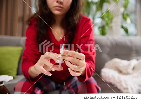 Young girl prepares drug for injection, removes air from syringe in order to painlessly give herself injection. 121203213