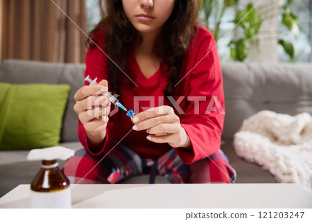 Young sick woman sits at table, unpack new syringe, prepares everything to make safe injection at home. Illness and treatment. 121203247