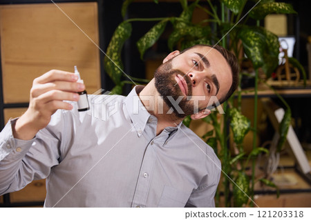 Young man suffering from ear pain and puts ear drops in them while sitting at work. Diseases and treatment. Young man suffering from ear pain and puts ear drops in them while sitting at work. Diseases and treatment. 121203318