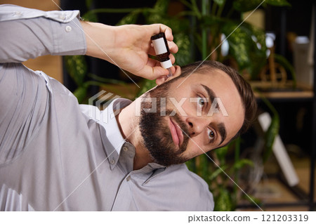 Young man suffering from ear pain and puts ear drops in them while sitting at work. Diseases and treatment. Young man suffering from ear pain and puts ear drops in them while sitting at work. Diseases and treatment. 121203319