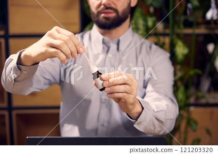 Young man holds medicine in his hands and opens it to put drops in his ears while sitting t des at work. Disease and treatment. 121203320
