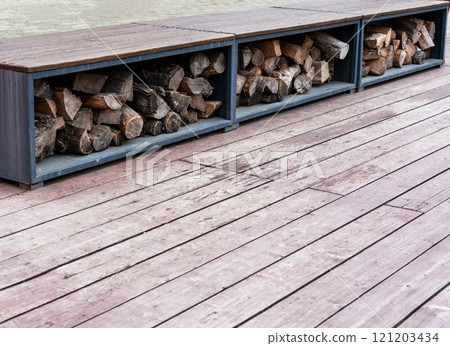 Modern outdoor wood storage integrated into wooden deck, featuring stacked firewood neatly arranged in metal compartments. stylish and functional element for outdoor living patio designs copy space Modern outdoor wood storage integrated into wooden deck, featuring stacked firewood neatly arranged in metal compartments. stylish and functional element for outdoor living patio designs copy space 121203434