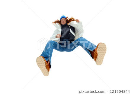 Young woman with red hair wearing white puffer jacket and blue beanie against white studio background. Bottom view 121204844