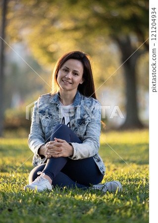 Woman sitting on grass in city park on summer day Woman sitting on grass in city park on summer day 121204934