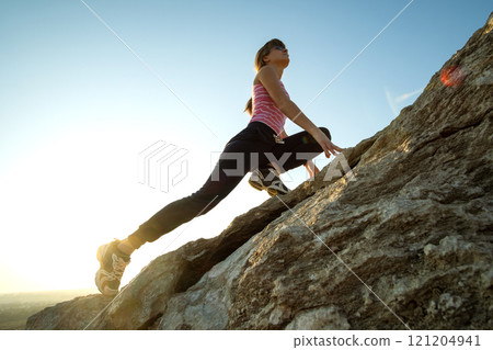 Woman hiker climbing steep big rock on a sunny day. Young female climber overcomes difficult climbing route. Active recreation in nature concept. Woman hiker climbing steep big rock on a sunny day. Young female climber overcomes difficult climbing route. Active recreation in nature concept. 121204941