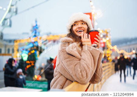 Woman with coffee in winter over outdoor ice skating rink on background. Winter holidays concept. 121204994