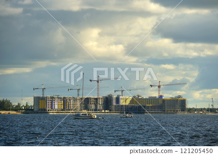 Tower cranes and frame structure of high residential apartment buildings at construction site on sea bay shore. Real estate development at waterfront 121205450