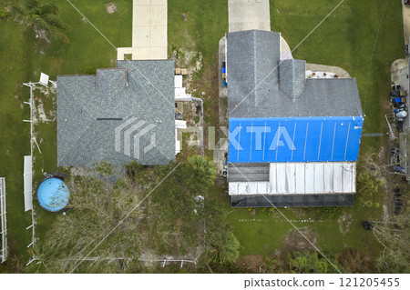 Top view of leaking house roof covered with protective tarp sheets against rain water leaks until replacement of asphalt shingles. Damage of building rooftop as aftermath of hurricane Ian in Florida Top view of leaking house roof covered with protective tarp sheets against rain water leaks until replacement of asphalt shingles. Damage of building rooftop as aftermath of hurricane Ian in Florida 121205455