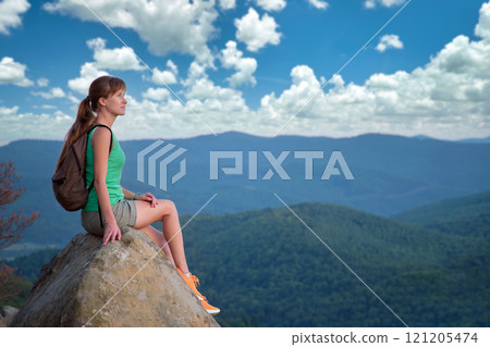 Tired hiker girl relaxing on rocky mountain top enjoying summer nature during travelling on wilderness trail. Lonely woman traveler traversing high hilltop route. Healthy lifestyle concept Tired hiker girl relaxing on rocky mountain top enjoying summer nature during travelling on wilderness trail. Lonely woman traveler traversing high hilltop route. Healthy lifestyle concept 121205474