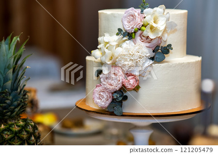Tall sweet wedding cake decorated with live pink and white flowers on a table. 121205479