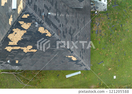 Ruined rooftop in need of repair. Wind damaged house roof with missing asphalt shingles after hurricane Ian in Florida Ruined rooftop in need of repair. Wind damaged house roof with missing asphalt shingles after hurricane Ian in Florida 121205588