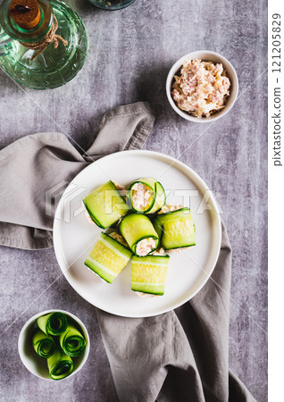 Cucumber rolls with fish salad on a plate on the table top and vertical view 121205829