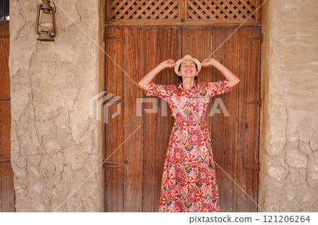 Young woman in an ethnic dress and hat exploring Al Seef Park in Dubai. Surrounded by traditional Emirati architecture and modern vibes, she enjoys the charm of Dubai Creek's cultural heritage. 121206264
