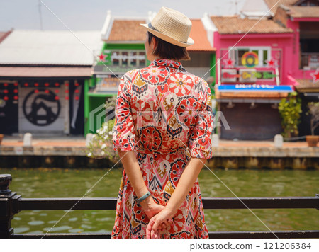 Young woman in ethnic dress and hat exploring the vibrant streets of Malacca, Malaysia. A blend of cultural heritage, colorful architecture, and tropical charm. Perfect travel and lifestyle moments. Young woman in ethnic dress and hat exploring the vibrant streets of Malacca, Malaysia. A blend of cultural heritage, colorful architecture, and tropical charm. Perfect travel and lifestyle moments. 121206384