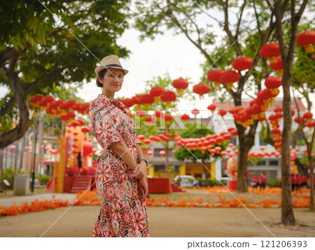 Young woman in ethnic dress and hat exploring the festive streets of George Town, Malaysia, during Chinese New Year. Vibrant lanterns, cultural celebrations, historic charm create unique atmosphere. 121206393