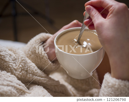Woman in a comfortable bathrobe enjoying a creamy coffee with milk, relishing a tranquil morning at home, embracing warmth and peace 121206798