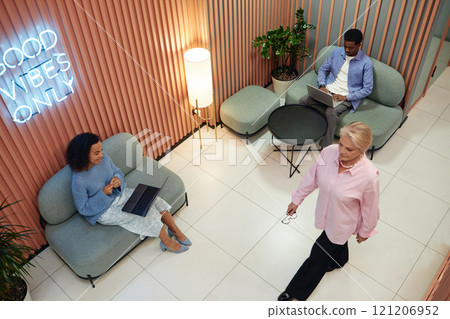 Wide angle shot of coworking lounge area where creative team working and video calling on laptops while sitting on comfy seats Wide angle shot of coworking lounge area where creative team working and video calling on laptops while sitting on comfy seats 121206952