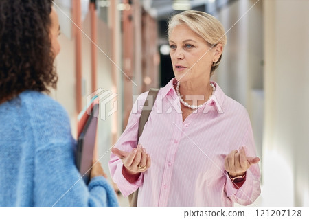 Portrait of elegant mature businesswoman wearing pink shirt outfit for office styled with golden jewelry talking to female colleague while meeting in hallway, copy space 121207128