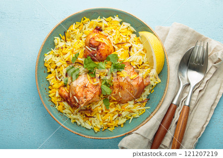 Traditional Indian dish chicken biryani with cilantro and lemon in a bowl top view on blue background 121207219