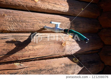 Garden Hose Nozzle on Wooden Wall in Sunlight 121208076