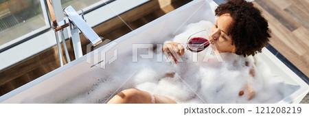 Website header shot of African American woman drinking red wine while lying in hot foamy water in bathtub enjoying pastime at home Website header shot of African American woman drinking red wine while lying in hot foamy water in bathtub enjoying pastime at home 121208219