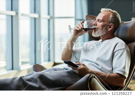 Side view of successful mature man drinking red wine while relaxing in comfy armchair indulging in delicious alcohol beverage on weekend at home, copy space Side view of successful mature man drinking red wine while relaxing in comfy armchair indulging in delicious alcohol beverage on weekend at home, copy space 121208227