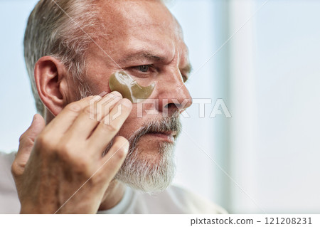 Portrait shot of concentrated senior man carefully applying hydrogel patch under eye lining mask with fingers during skin care routine at home, copy space Portrait shot of concentrated senior man carefully applying hydrogel patch under eye lining mask with fingers during skin care routine at home, copy space 121208231