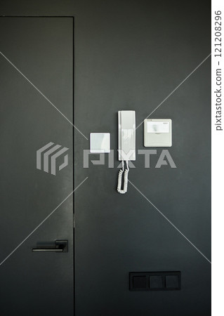 Vertical shot of intercom electronic panel and handset with microphone for talking to guests hanging on black wall inside minimalist apartment in residential building, copy space Vertical shot of intercom electronic panel and handset with microphone for talking to guests hanging on black wall inside minimalist apartment in residential building, copy space 121208296